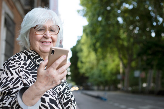 Older Woman Looking At Her Cell Phone On The Street