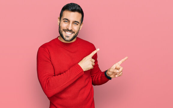 Young Hispanic Man Wearing Casual Clothes Smiling And Looking At The Camera Pointing With Two Hands And Fingers To The Side.