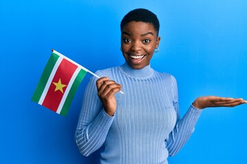 Young african american woman holding suriname flag celebrating achievement with happy smile and...