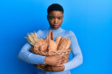 Young african american woman holding wicker basket with bread skeptic and nervous, frowning upset...