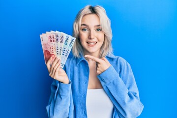 Young blonde girl holding new taiwan dollars banknotes smiling happy pointing with hand and finger