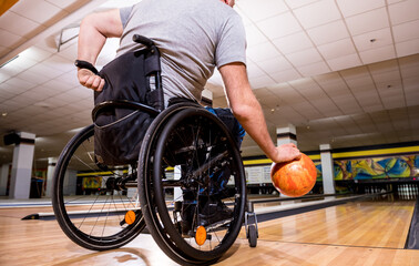 Young disabled man in wheelchair playing bowling in the club