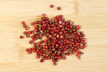 Red or pink peppercorns on light bamboo wooden cutting board background
