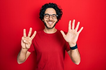 Handsome hispanic man wearing casual t shirt and glasses showing and pointing up with fingers number eight while smiling confident and happy.