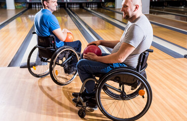 Two young disabled men in wheelchairs playing bowling in the club