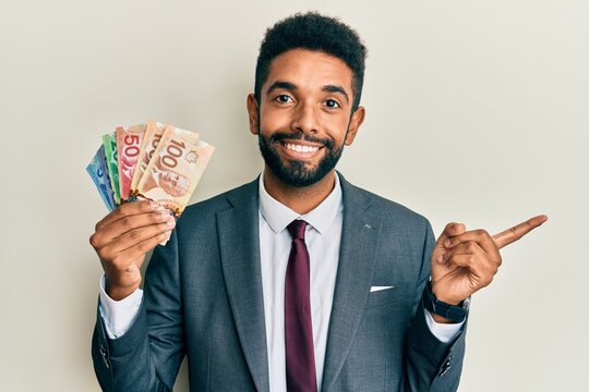 Handsome hispanic business man with beard holding canadian dollars smiling happy pointing with hand and finger to the side