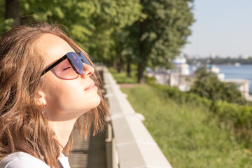 Beautiful young woman wearing sunglasses with closed eyes enjoying the sun. Concept of wellbeing, happiness, joyful, freedom and mental health.