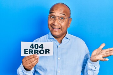 Middle age latin man holding paper with 404 error message celebrating achievement with happy smile...