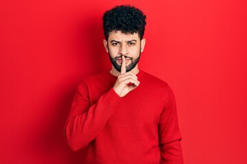 Young arab man with beard wearing casual red sweater asking to be quiet with finger on lips. silence and secret concept.