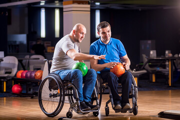 Two young disabled men in wheelchairs playing bowling in the club