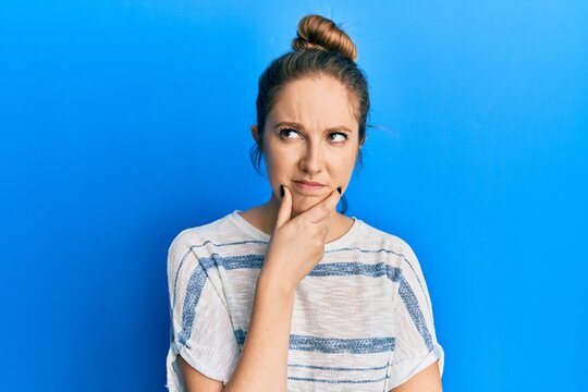 Young blonde woman wearing casual striped t shirt thinking concentrated about doubt with finger on chin and looking up wondering