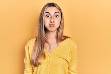 Obraz premium Beautiful hispanic woman wearing casual yellow sweater puffing cheeks with funny face. mouth inflated with air, crazy expression.