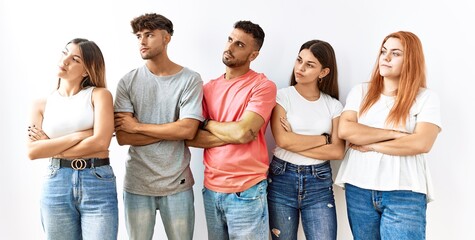 Group of young friends standing together over isolated background looking to the side with arms crossed convinced and confident
