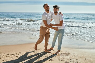 Young gay couple smiling happy dancing at the beach.