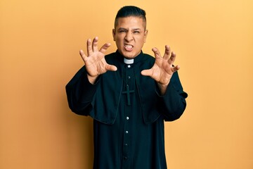 Young latin priest man standing over yellow background smiling funny doing claw gesture as cat,...