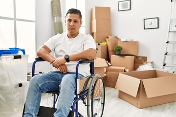 Young hispanic man sitting on wheelchair at new house with serious expression on face. simple and...