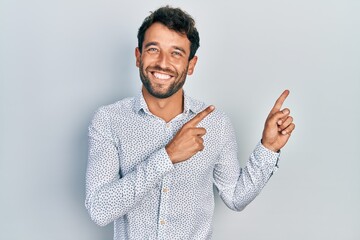 Handsome man with beard wearing casual elegant shirt smiling and looking at the camera pointing with two hands and fingers to the side.