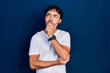 Young hispanic man wearing casual white t shirt serious face thinking about question with hand on...