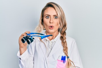 Beautiful young blonde woman holding scientist glasses scared and amazed with open mouth for surprise, disbelief face