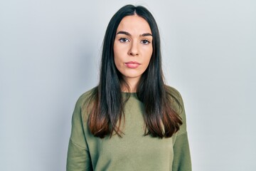 Young brunette woman wearing casual green sweater with serious expression on face. simple and natural looking at the camera.