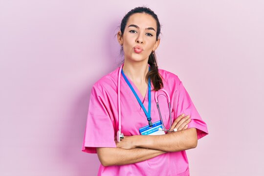 Young brunette woman wearing doctor uniform and stethoscope standing with arms crossed looking at the camera blowing a kiss being lovely and sexy. love expression.
