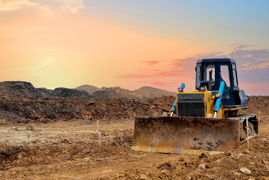 Dozer on land clearing, grading, pool excavation, utility trenching. Earth-moving equipment. Bulldozer at road construction on sunset background. Leveling ground in open pit. Mining industry concept