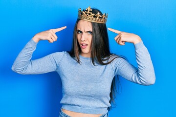 Young brunette teenager wearing princess crown clueless and confused expression. doubt concept.