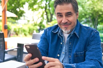 Outdoor portrait of white man using smartphone, looking at camera.