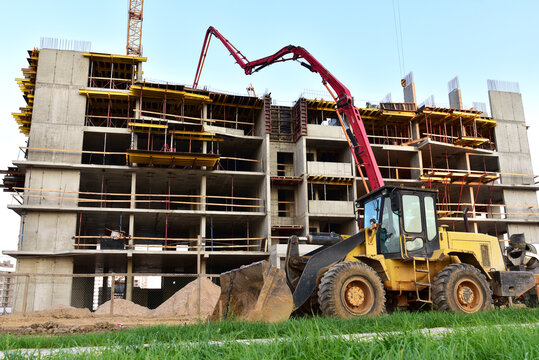 Formworks and pouring concrete through a сoncrete pump truck connected to a ready-mixed truck. Wheel loader at construction site. Tower cranes construct residential building