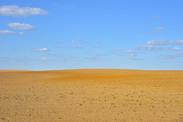 View of a deserted sand field against a blue sky with clouds. - Powered by Adobe