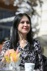 Smiling stylish woman in black shirt sitting at the table drinking coffee in the terrace of restaurant.