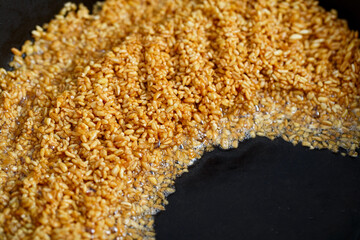 Fried golden bulgur in a frying pan close-up. Caramel flavored wheat grains stirring in boiling oil
