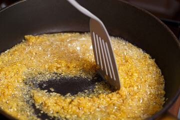 Fried bulgur in a frying pan. Caramel flavored wheat grains stirring with a kitchen spatula in...