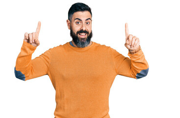 Fototapeta premium Hispanic man with beard wearing casual winter sweater smiling amazed and surprised and pointing up with fingers and raised arms.