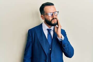 Young man with beard wearing business suit and tie touching mouth with hand with painful expression because of toothache or dental illness on teeth. dentist