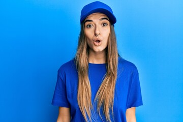Young hispanic woman wearing delivery uniform and cap scared and amazed with open mouth for surprise, disbelief face