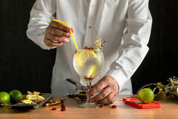  Barman standing behind and holding freshly prepared gin and tonic on a wooden table