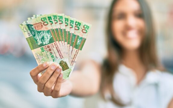 Beautiful latin teenager girl smiling happy holding hong kong dollars at the city.