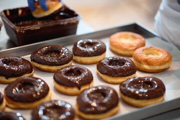 A worker is topping donuts with chocolate topping in a candy workshop. Pastry, dessert, sweet, making