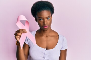 Young african american girl holding pink cancer ribbon thinking attitude and sober expression...