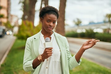Young african american reporter woman using microphone at the city