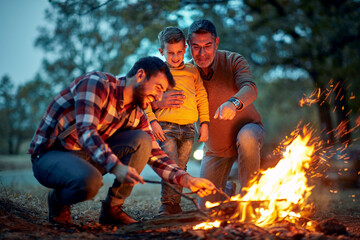 Grandfather and father in the forest showing to grandson how to light up a campfire
