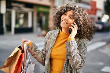 Young hispanic woman going shopping and talking on the smatphone at the city.