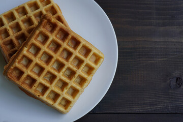 Warm waffles in a white plate on a black wooden table                 