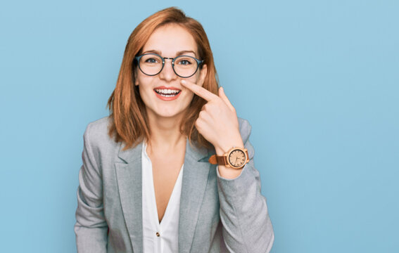 Young caucasian woman wearing business style and glasses pointing with hand finger to face and nose, smiling cheerful. beauty concept