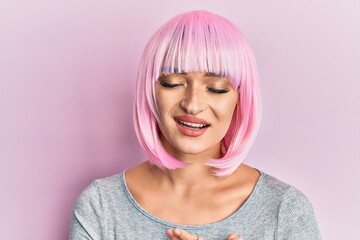 Young caucasian woman wearing pink wig smiling with hands on chest with closed eyes and grateful gesture on face. health concept.