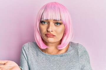 Young caucasian woman wearing pink wig clueless and confused expression with arms and hands raised....