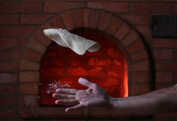a baker's hand with a tortilla on the background of a stone oven for cooking