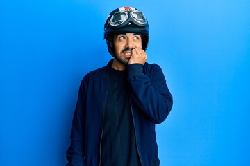Young hispanic man holding motorcycle helmet looking stressed and nervous with hands on mouth biting nails. anxiety problem.
