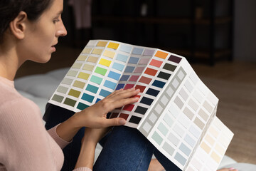 Back rear side view concentrated creative young woman sitting on sofa, holding paint swatches...